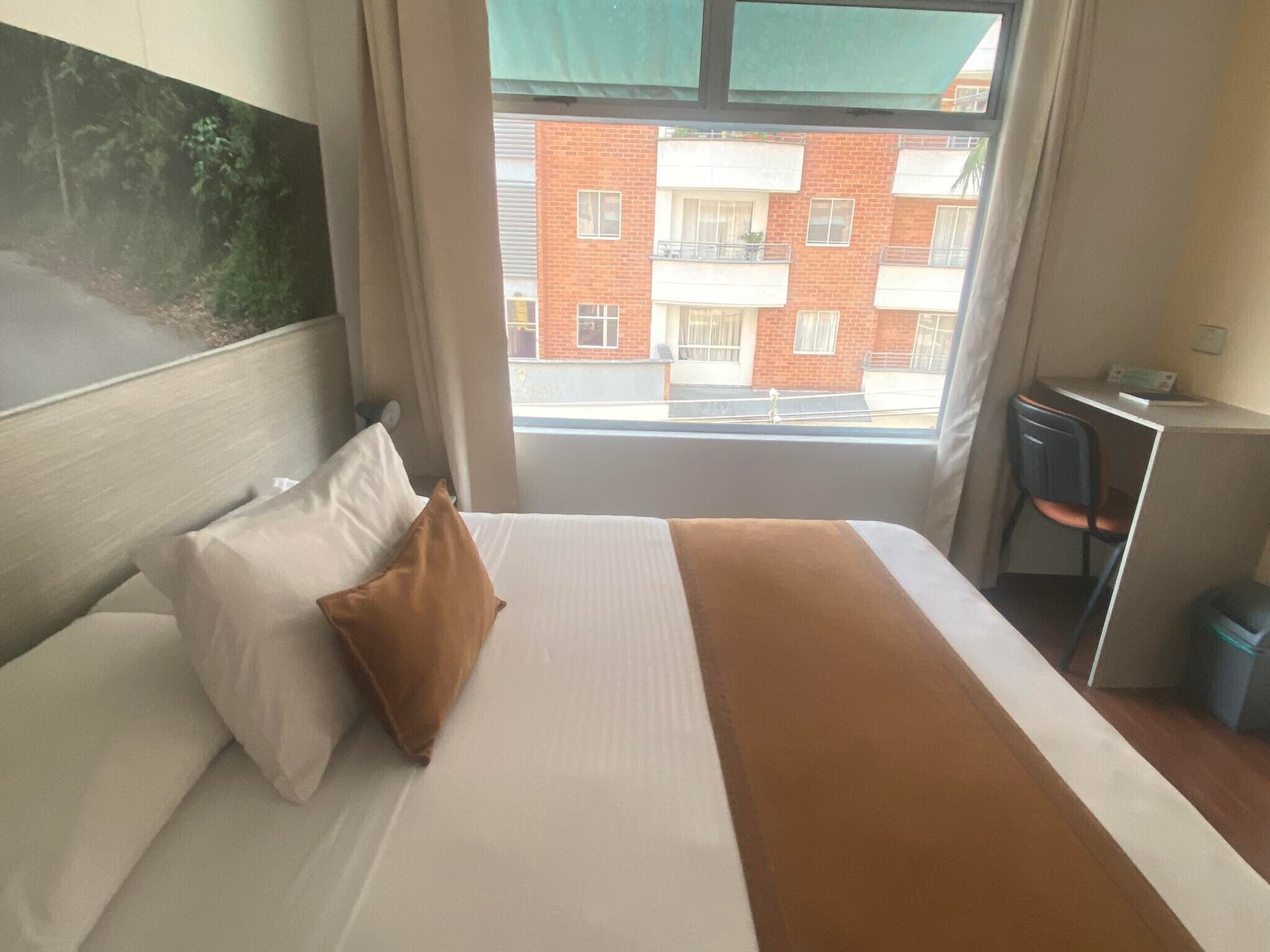 A hotel room with a bed, a desk, and a view of a red brick building with balconies.