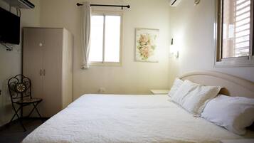 Un dormitorio con cama, armario, silla, ventana con cortinas y un cuadro colgado en la pared.