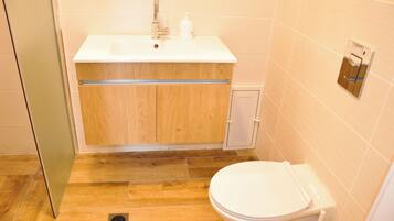 Un baño con lavamanos blanco, mueble de madera y un inodoro.