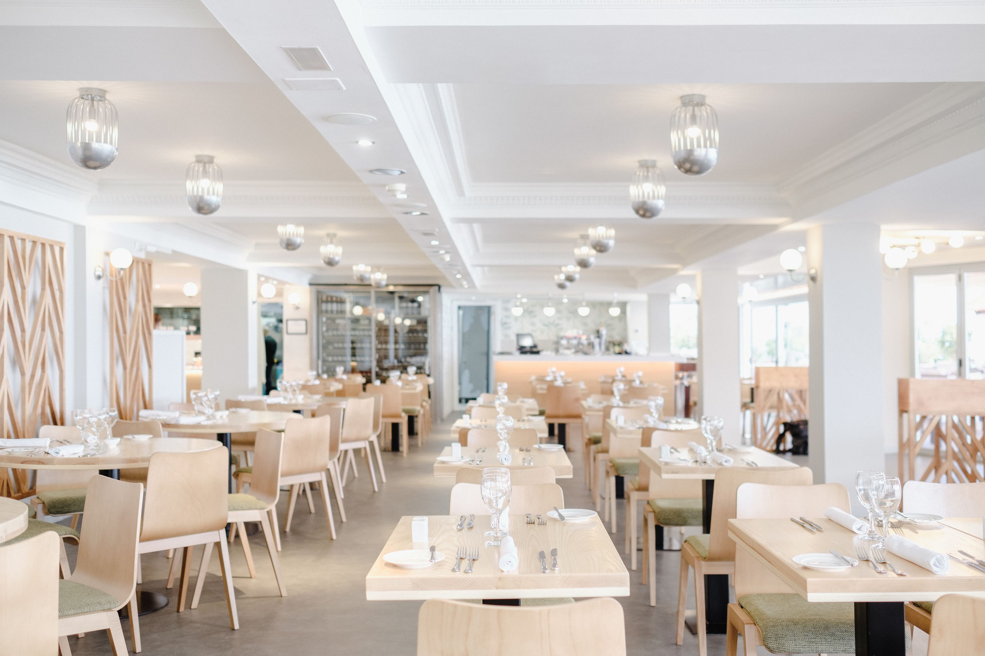 Un restaurant moderne avec des tables et des chaises disposées avec soin, un éclairage au plafond et un design épuré et minimaliste.