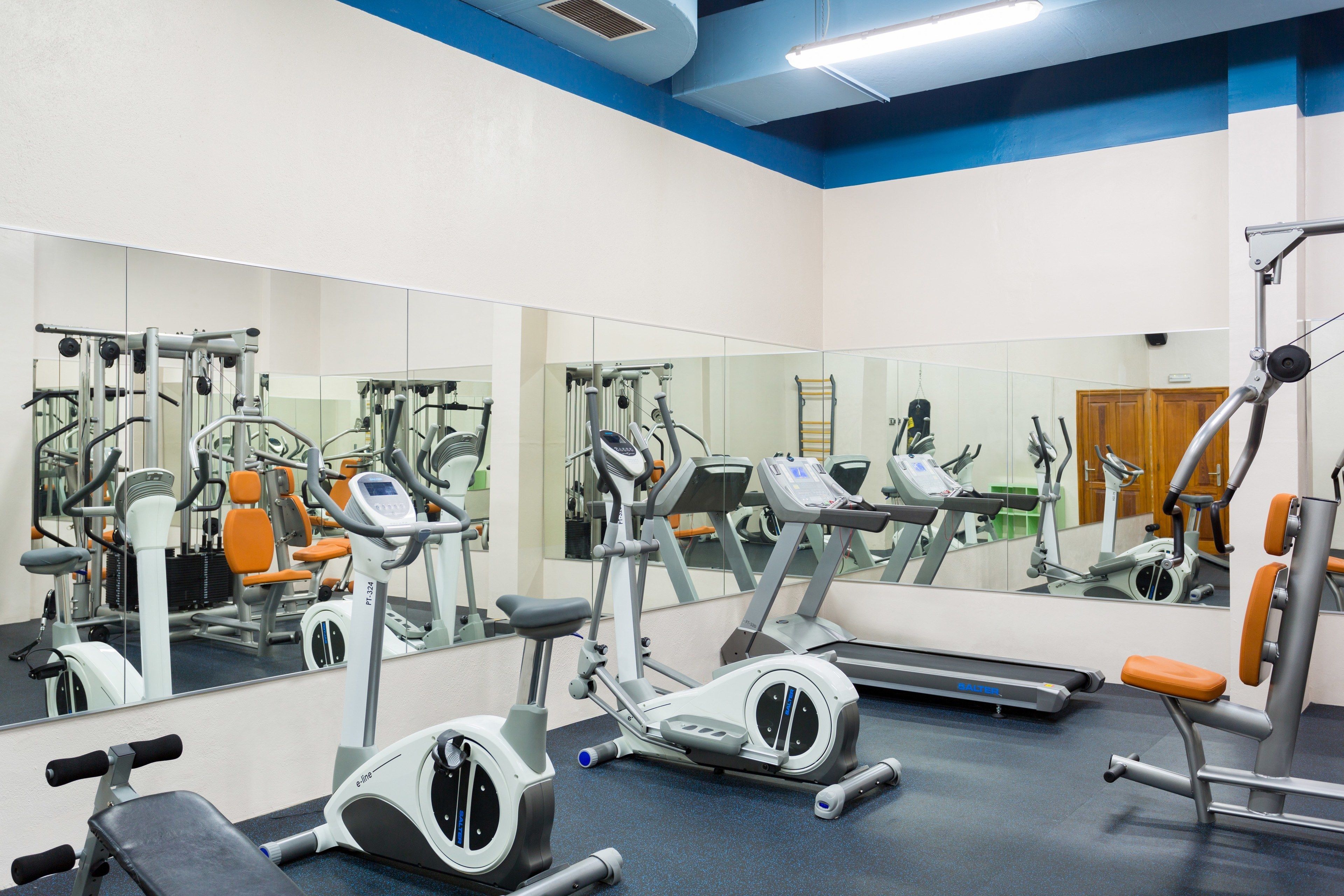 Un gimnasio con equipo de ejercicio, espejos y techo azul.