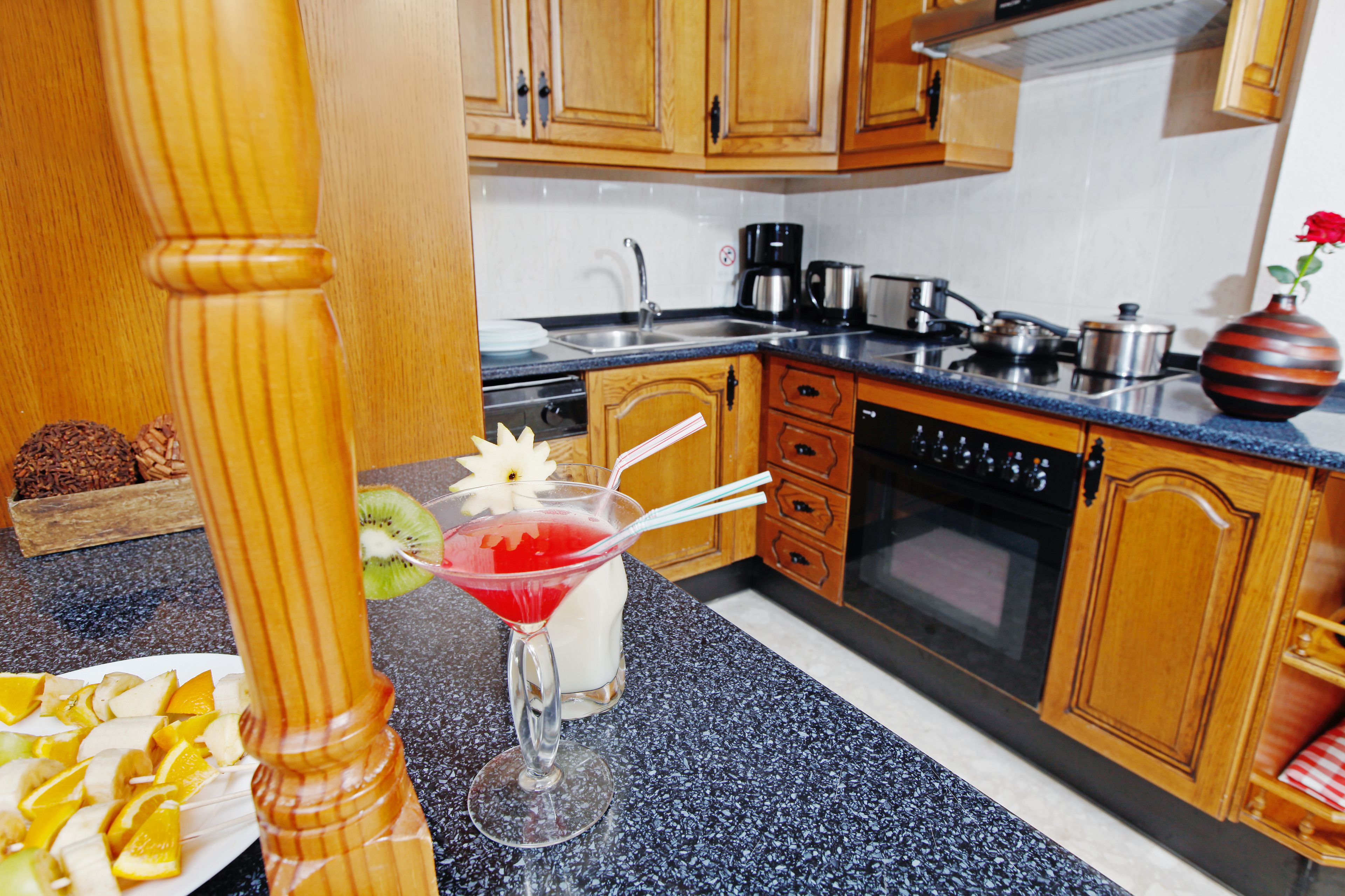 A kitchen with wooden cabinets, a granite countertop, a coffee maker, and a vase with a flower.