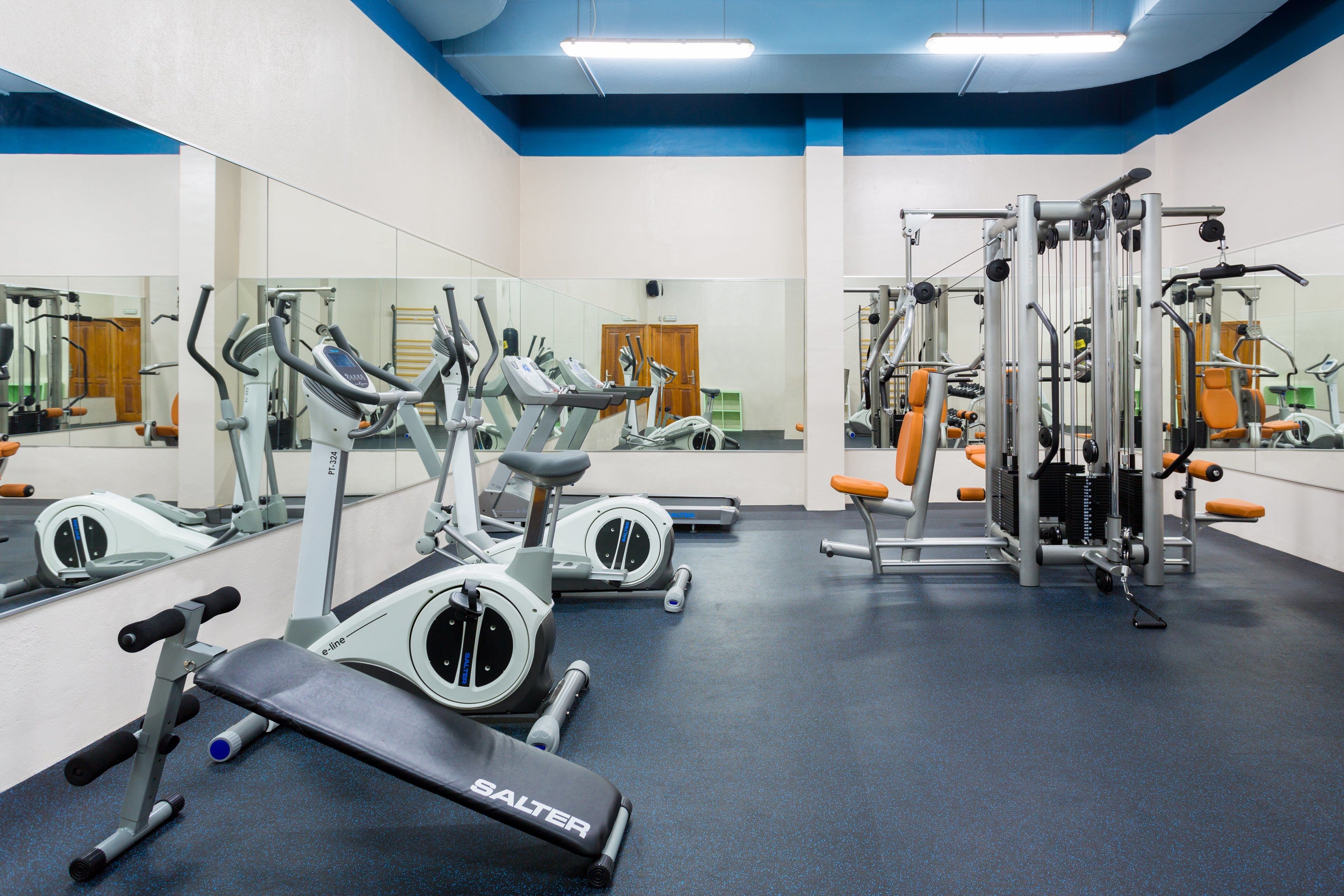 A gym with exercise equipment, mirrors, and a blue and white color scheme.