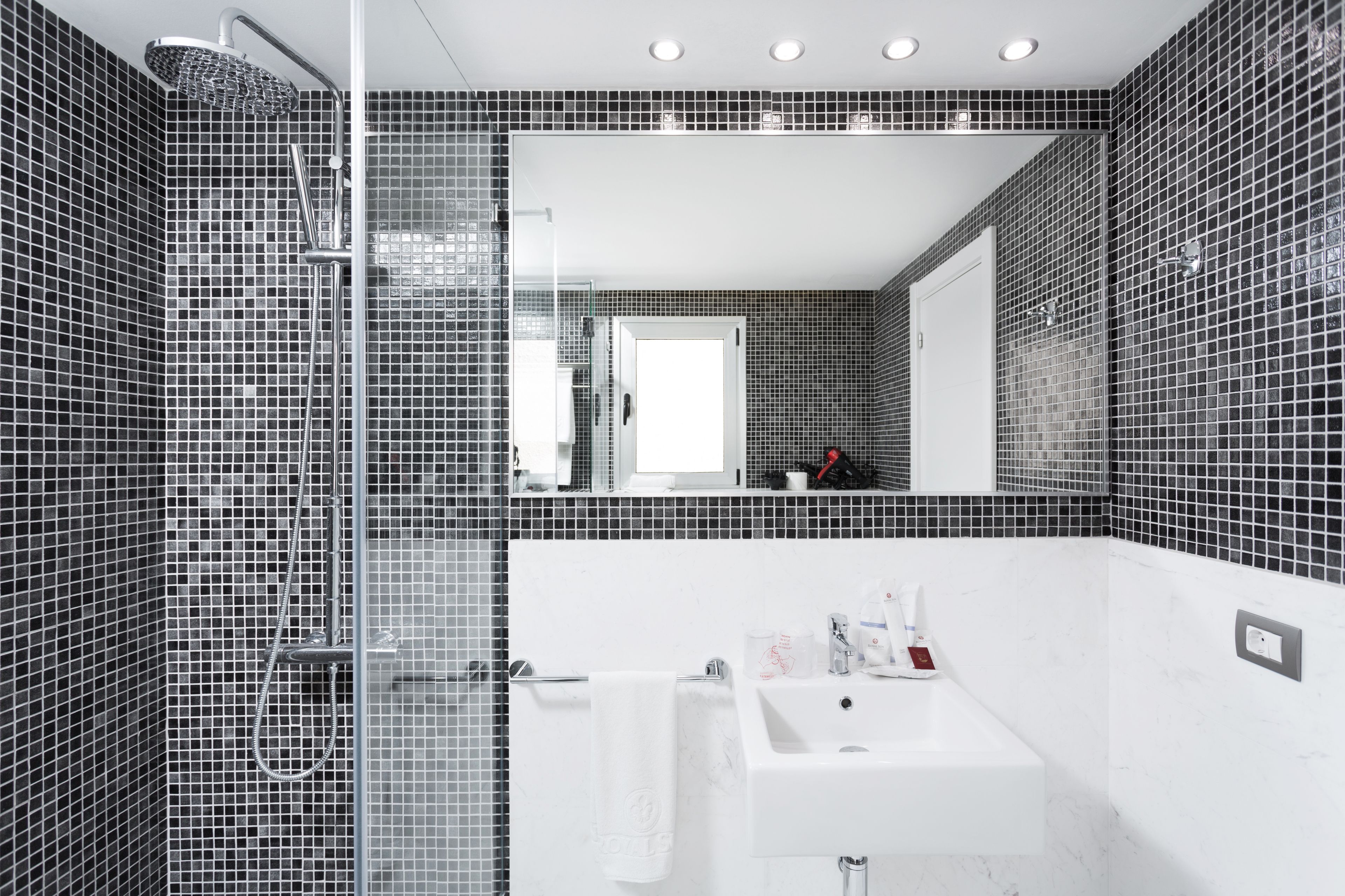Ein modernes Badezimmer mit einer gläsernen Dusche, einem weißen Waschbecken und einem großen Spiegel.