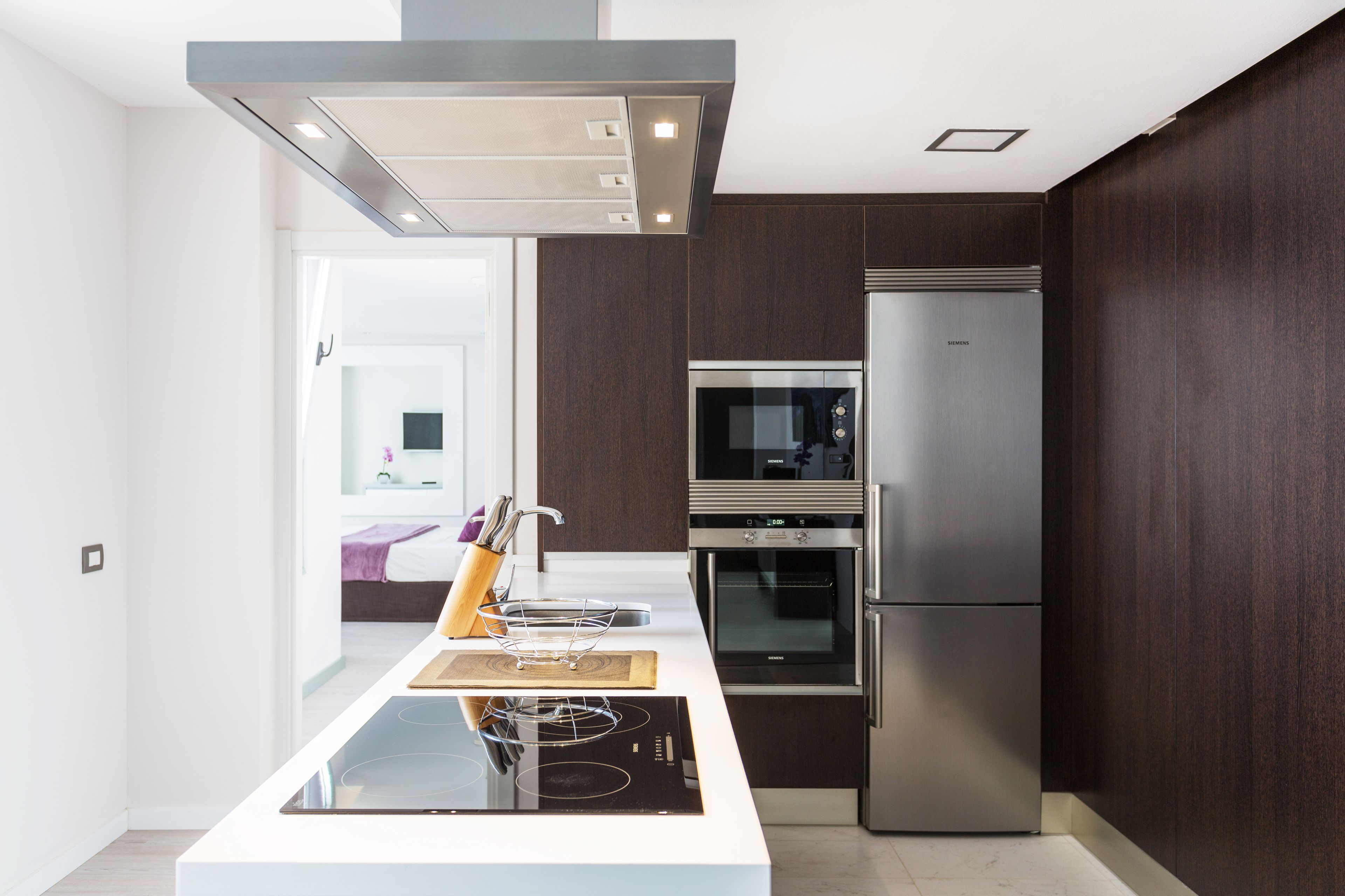 Une cuisine moderne dotée d’un îlot central, d’appareils électroménagers en acier inoxydable et de lambris en bois foncé.