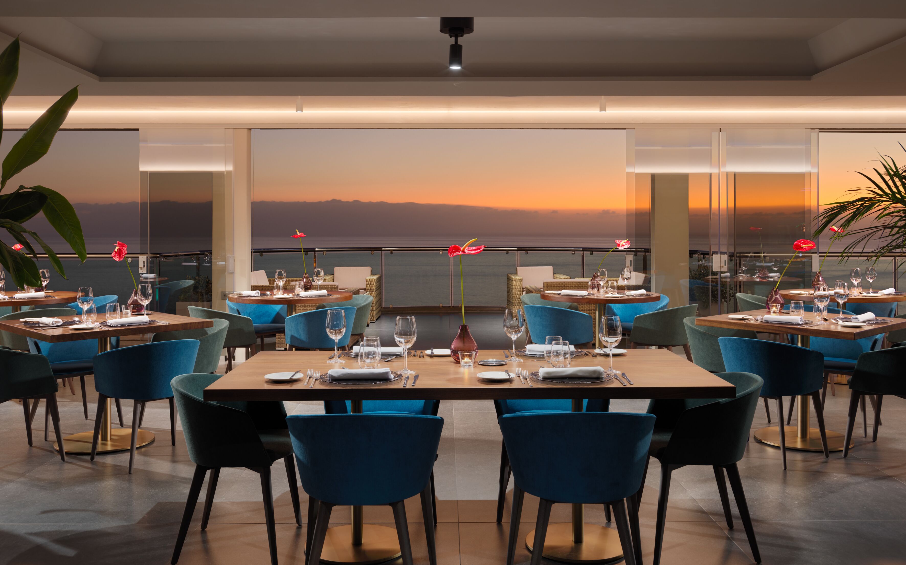 Un restaurant où les tables sont dressées pour le service, de grandes fenêtres offrant une vue sur l’océan et un décor intérieur moderne.