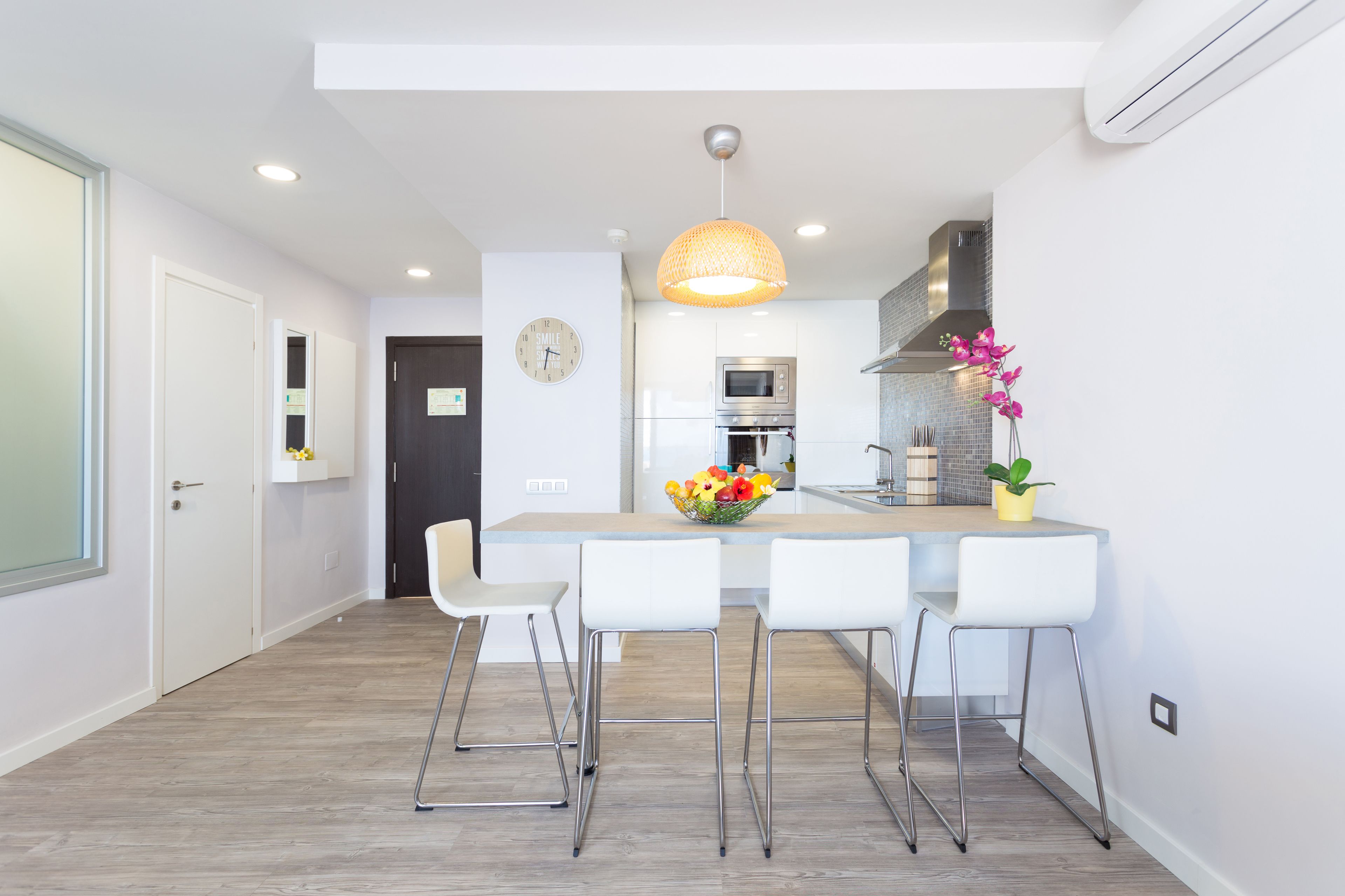 A modern kitchen with white cabinetry, a central island with bar stools, a hanging pendant light, and a clock on the wall.