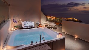 Zona de spa con hidromasaje, toallas y velas, con vistas a un paisaje urbano al anochecer.