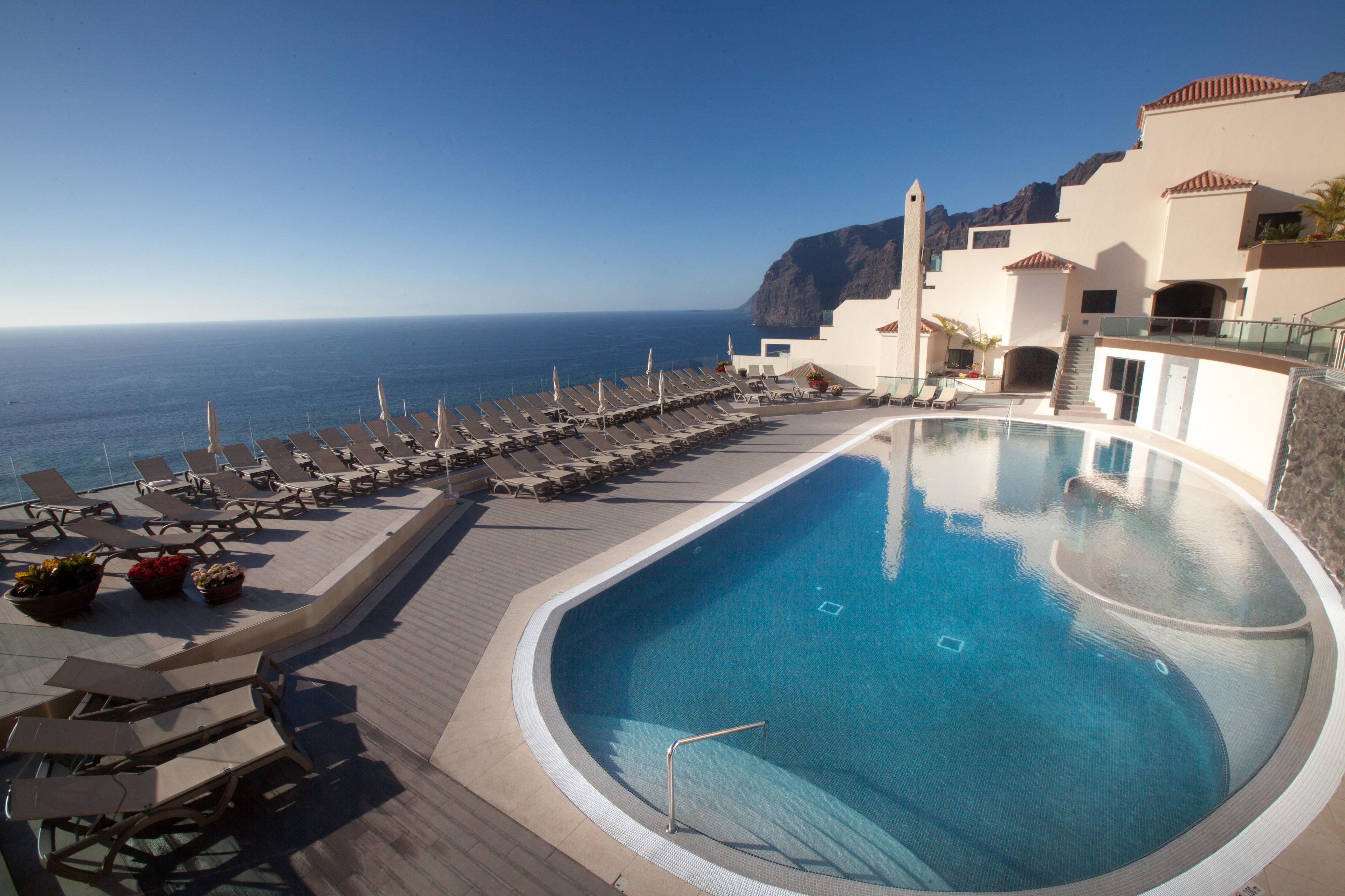 A pool area with lounge chairs and a view of the ocean.