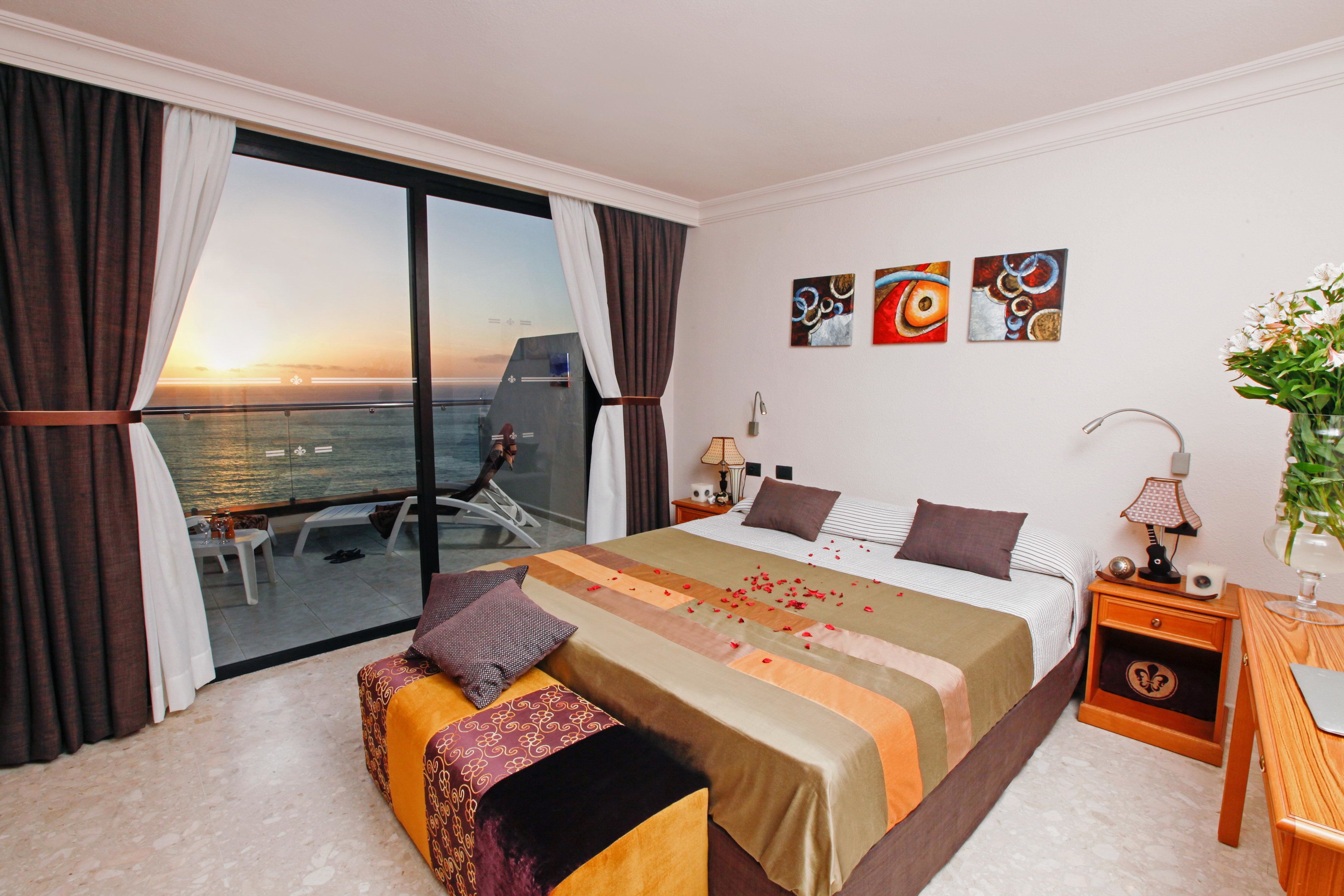 Ein Hotelzimmer mit einem großen Bett, einer Couch, einem Balkon mit Meerblick und Bildern an der Wand.