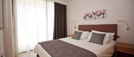 A hotel room with a large bed, a nightstand, a painting on the wall, and a window with curtains.