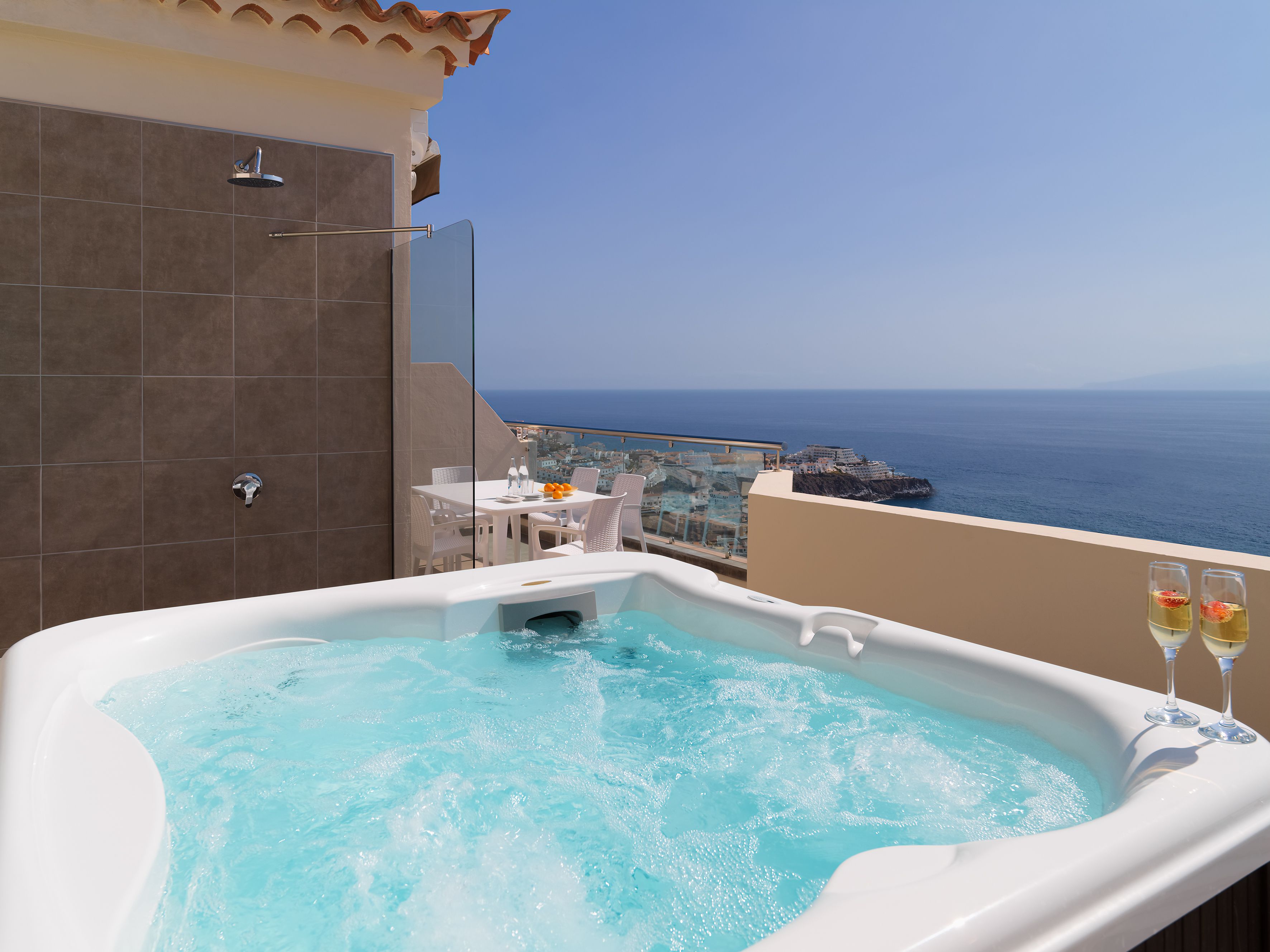 A hot tub with a clear view of the sea and a table with chairs.