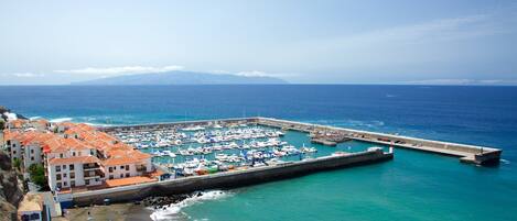 A coastal marina with boats, a pier, and buildings with red-tiled roofs.