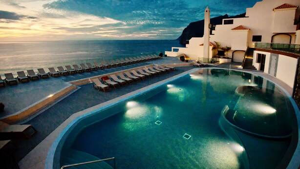 Una piscina con tumbonas y vistas al mar al atardecer.