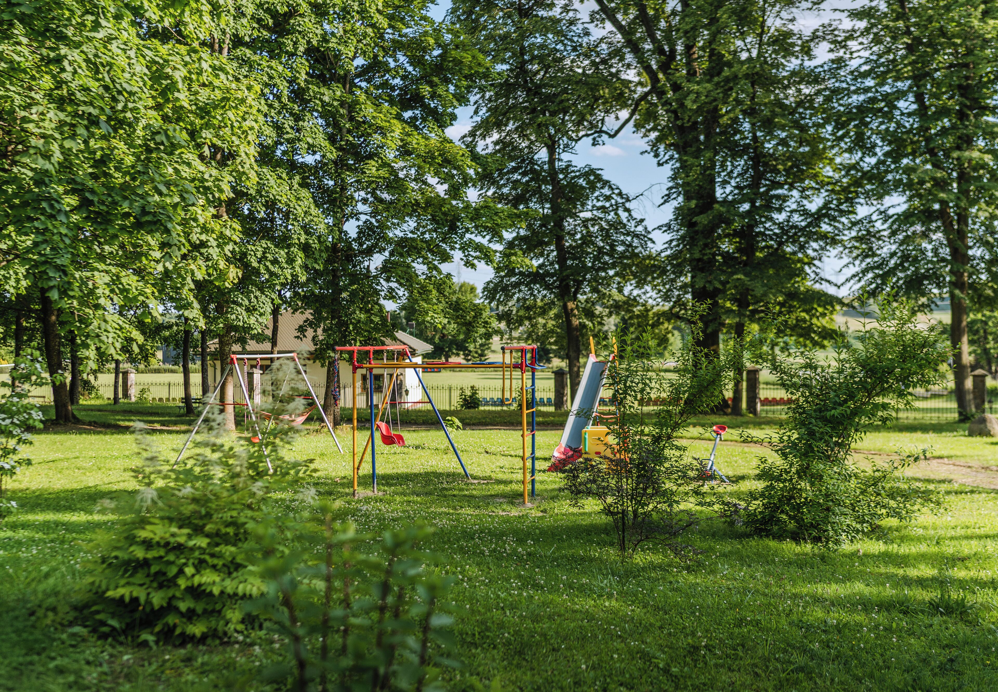 A playground with swings and slides, surrounded by trees and grass.