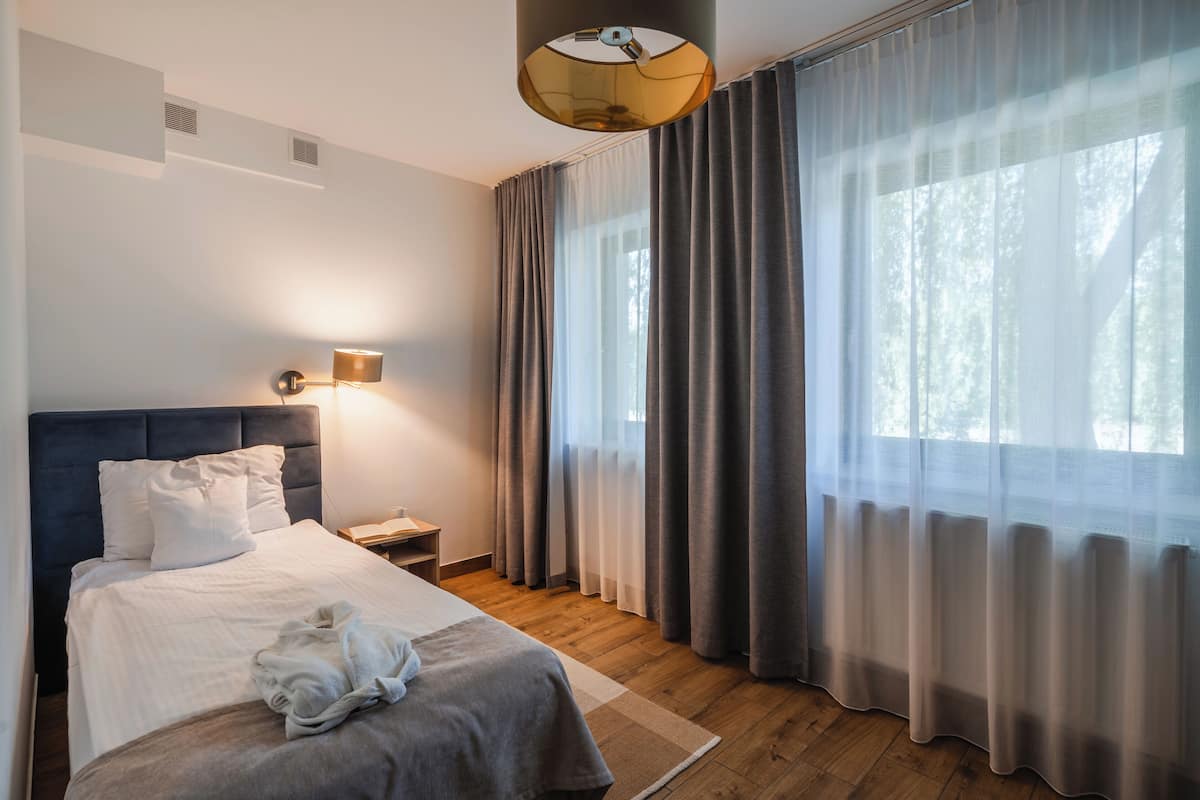 A bedroom with a bed, bedside table, lamp, and curtains.