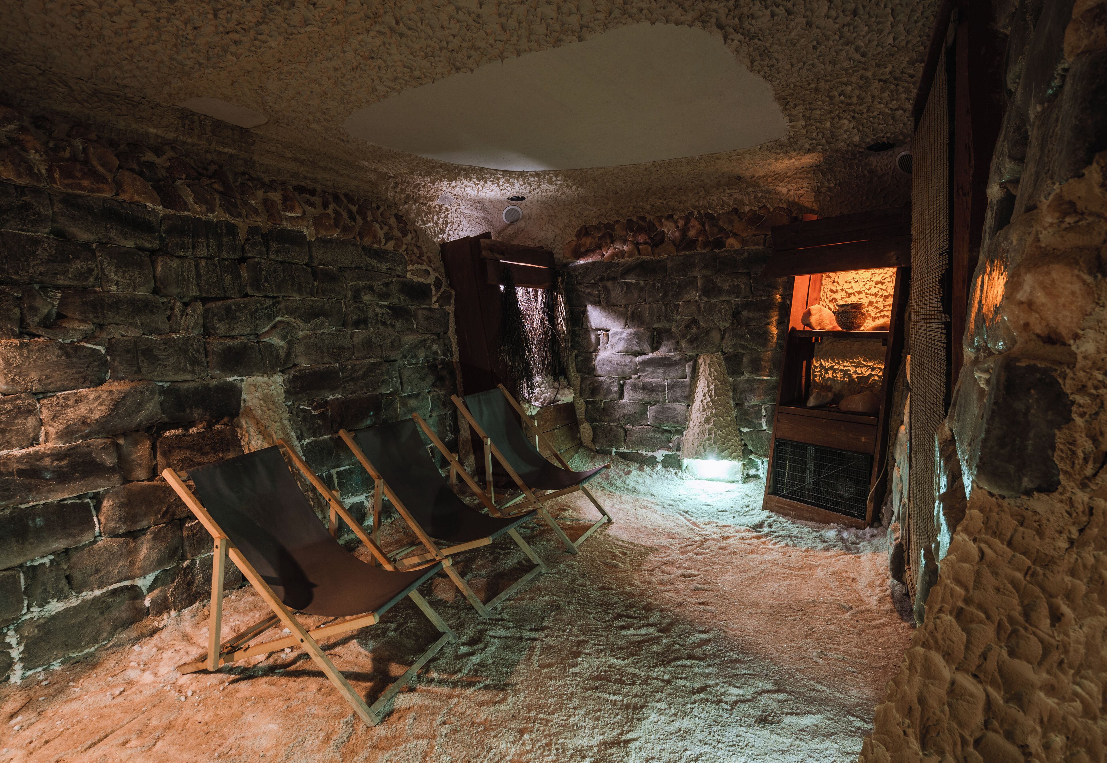 Una habitación con paredes de piedra, chimenea, sillas de madera y un ambiente rústico.