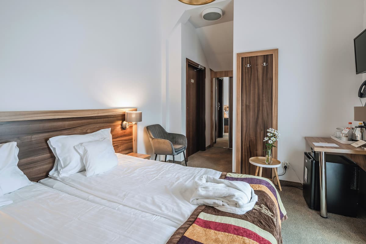 A hotel room with a large bed, a desk, a chair, and a small refrigerator.