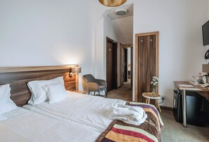 A hotel room with a large bed, a desk, a chair, and a small refrigerator. - Dwór Kombornia Folwark (Korczyna)