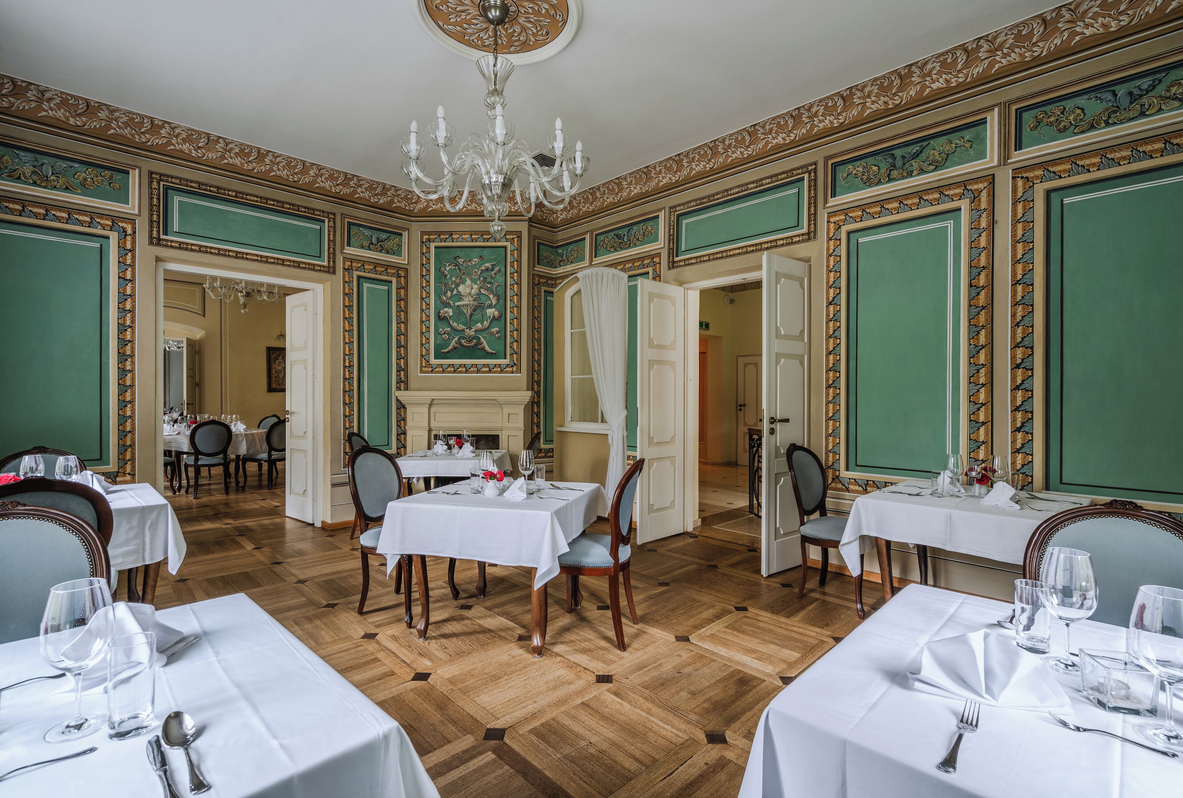 Un comedor con varias mesas dispuestas para el servicio, una araña y decoraciones ornamentales en las paredes.