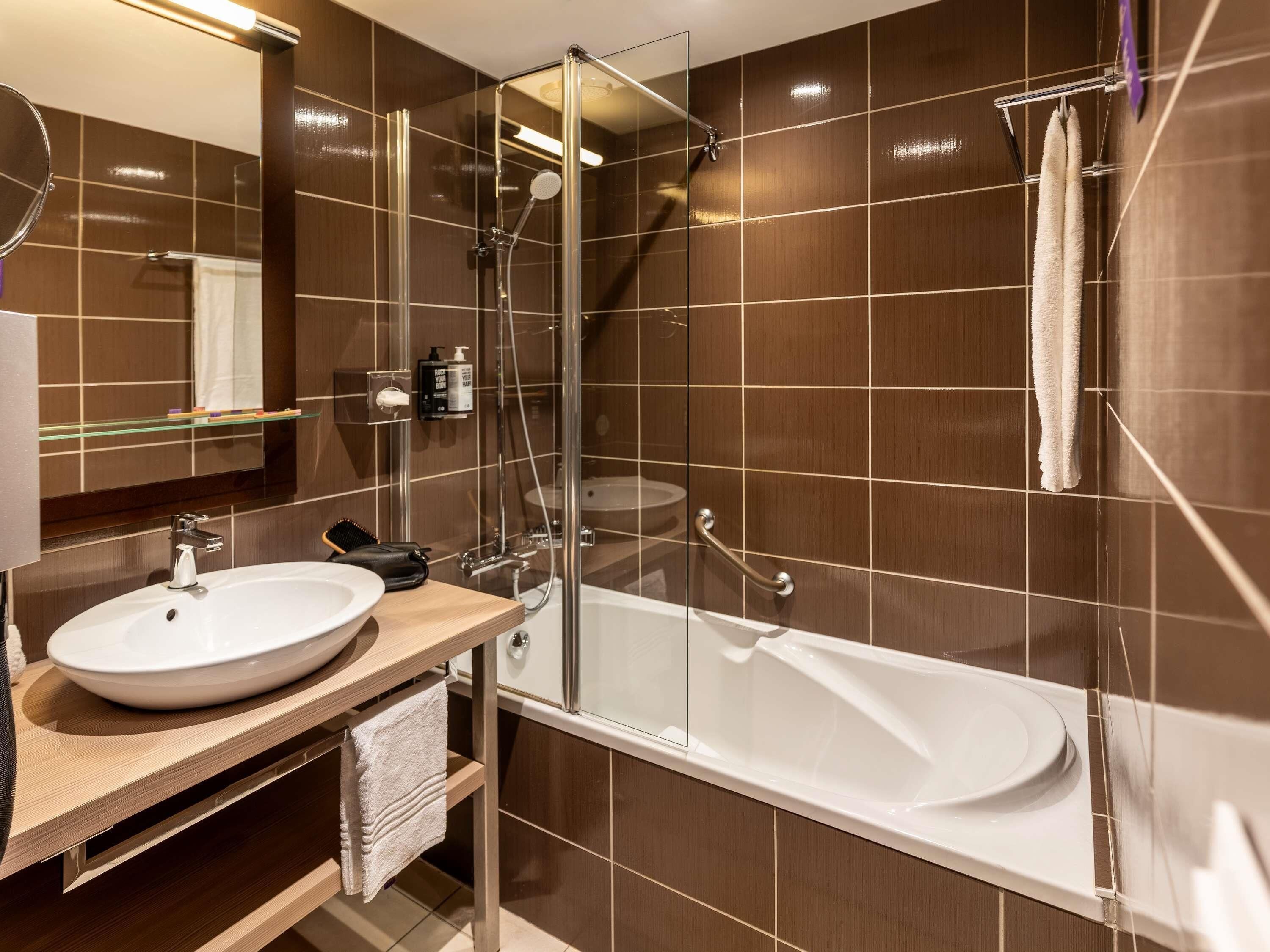 Un baño moderno con ducha de vidrio, bañera blanca y tocador de madera con lavabo.