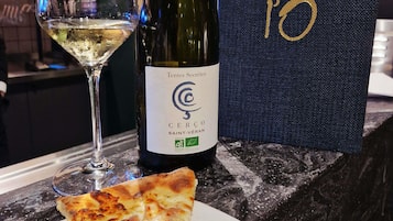 Uma garrafa de vinho, um copo de vinho branco e uma fatia de pizza em uma bancada de mármore.