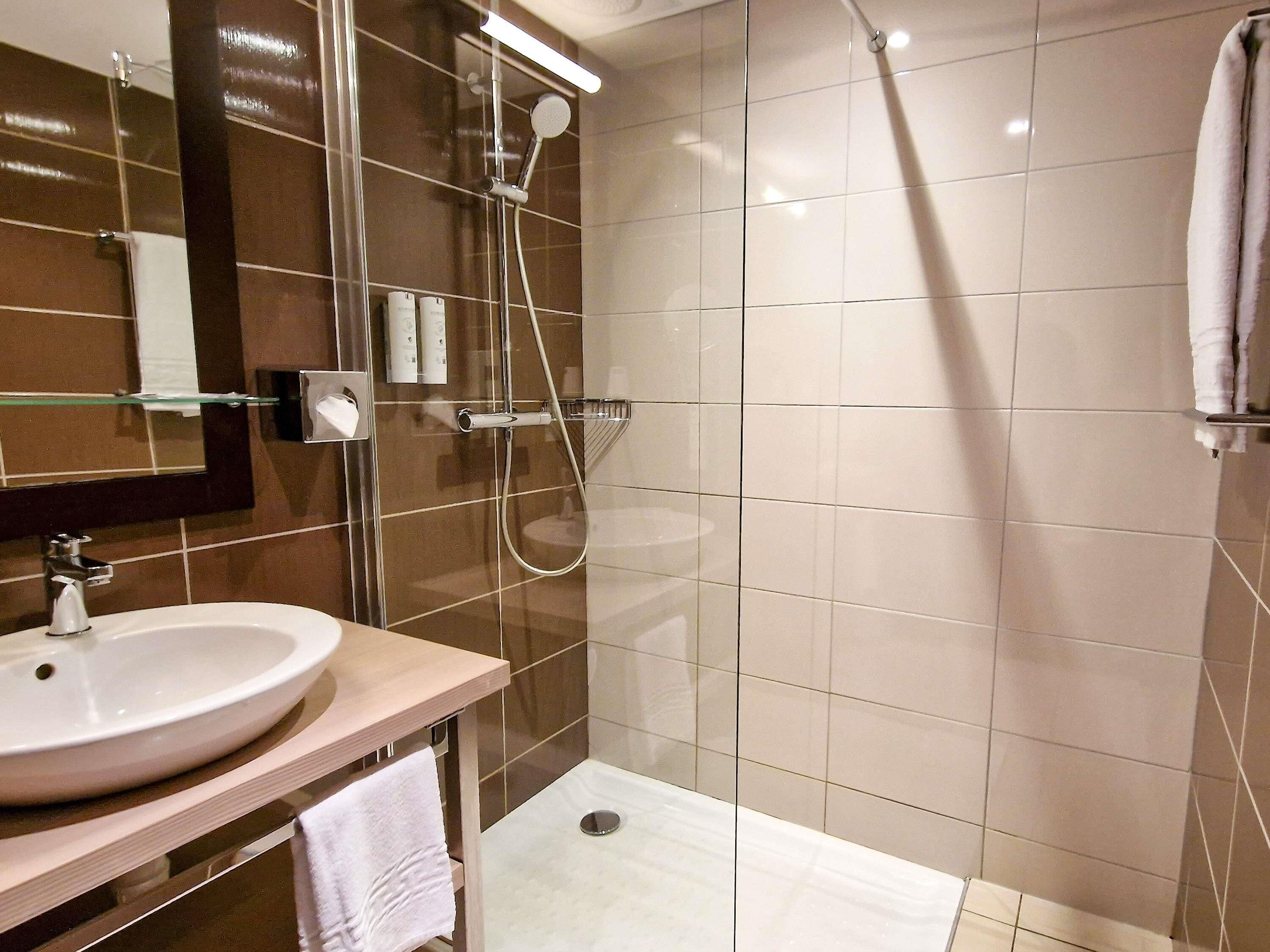 Un baño con lavamanos, espejo, ducha y toallero.