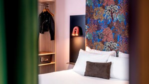 Een hotelkamer met een bed, een garderobe en een muur met een kleurrijk bloemenpatroon.