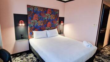 A hotel room with a bed, two wall-mounted lamps, a colorful floral headboard, and a door.