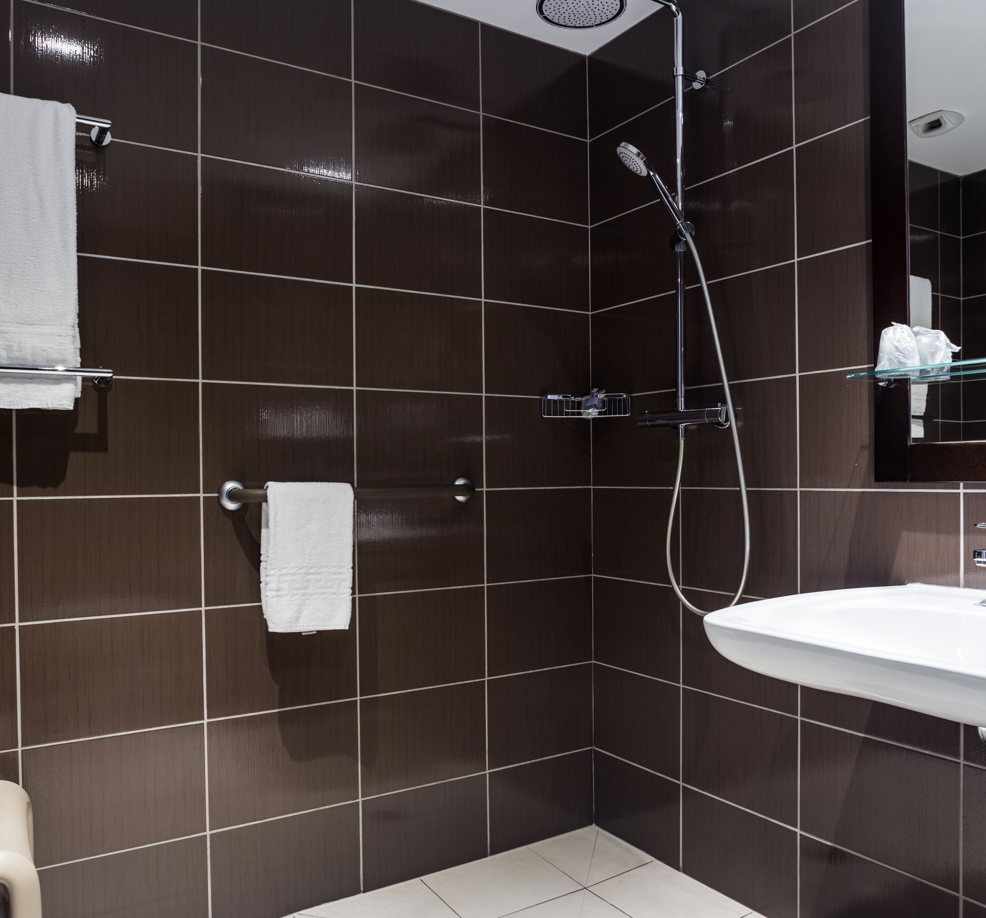 Ein modernes Badezimmer mit dunkel gefliesten Wänden, einem weißen Waschbecken und einer Dusche mit Duschbrause.