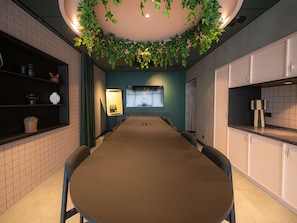 Une salle de conférence équipée d’une longue table, de chaises, d’un écran de projection et d’une étagère murale agrémentée d’objets décoratifs.