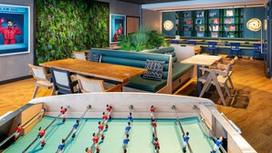 Een moderne binnenruimte met zithoeken, een tafelvoetbaltafel en een wand met een groen, weelderig ontwerp.