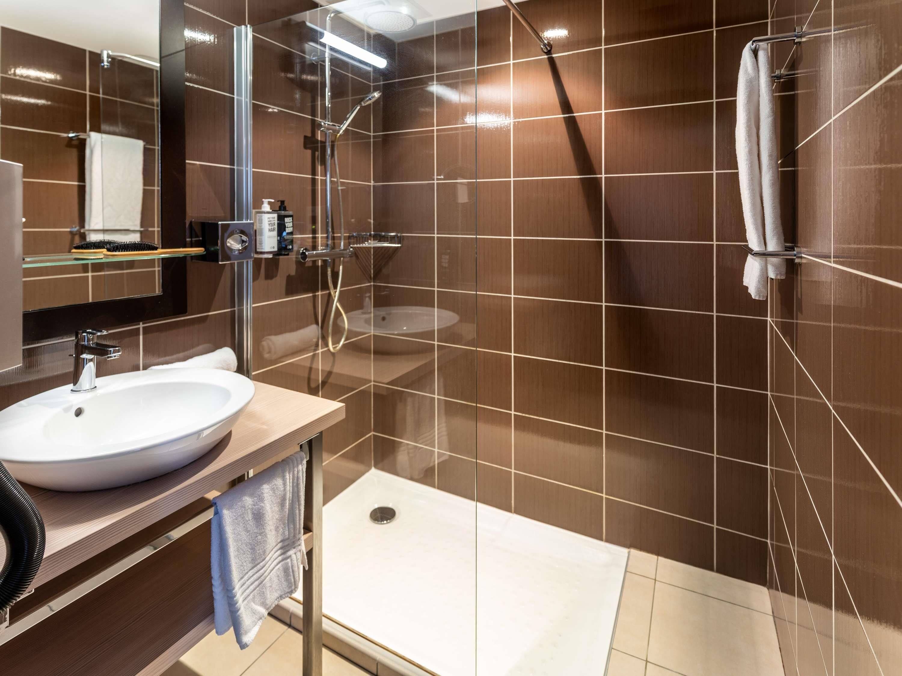 Ein modernes Badezimmer mit großem Spiegel, Waschbecken, Dusche und Toilette.