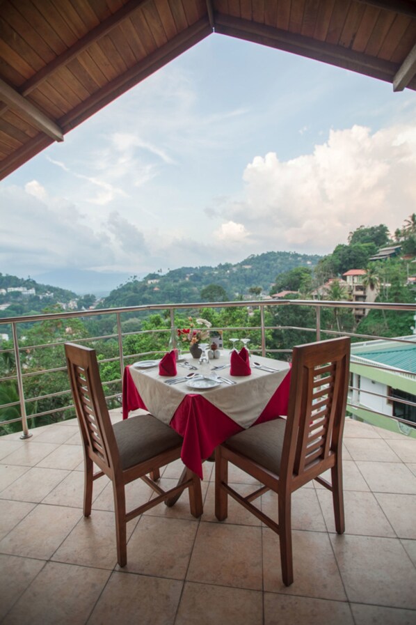 A dining table with two chairs, set for two, on a balcony with a view of a hilly landscape. - Senani Hotel (Kandy)