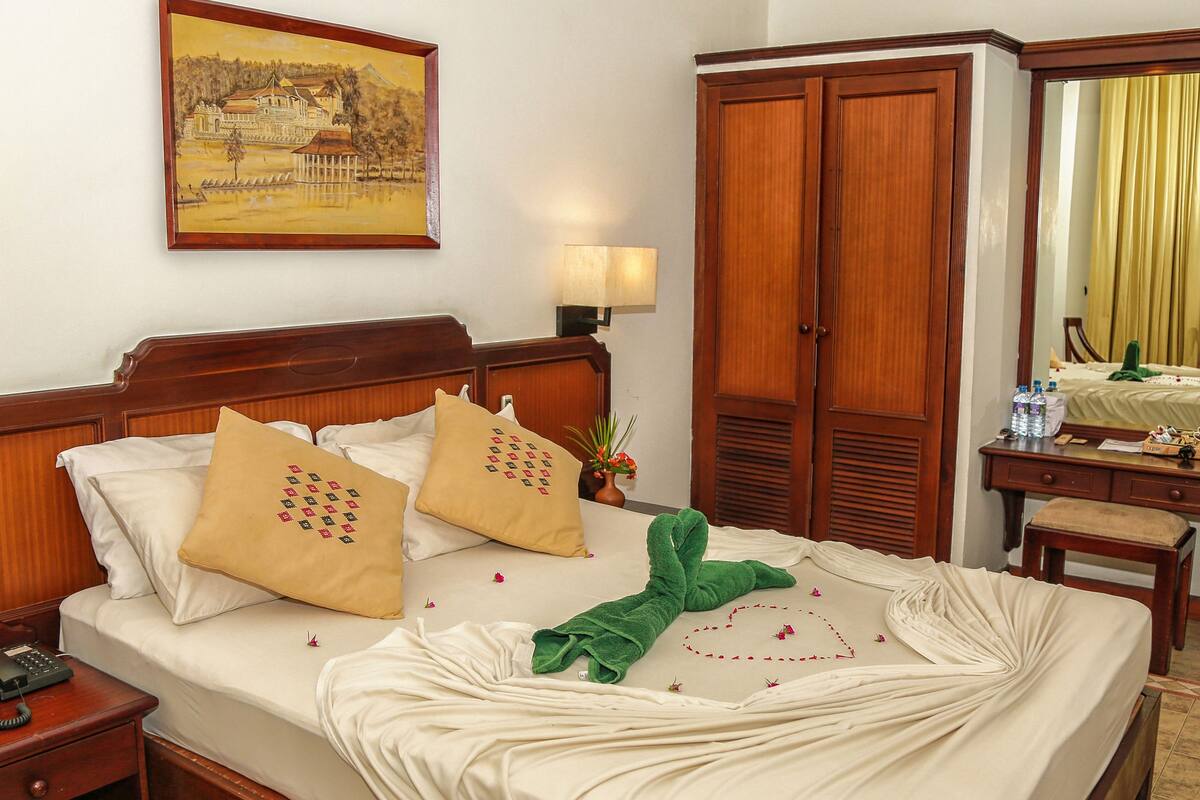 A hotel room with a bed, bedside tables, a desk, a mirror, and a painting on the wall.