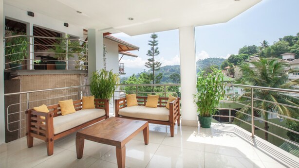 Un balcón amplio con sofá y mesa de madera, rodeado de plantas en macetas y con vistas a un paisaje exuberante.
