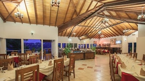Un restaurante con vigas de madera y un techo alto, mesas dispuestas con manteles rojos y sillas, y vistas al exterior.