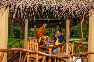 Un comedor de madera con techo de paja, rodeado de follaje.