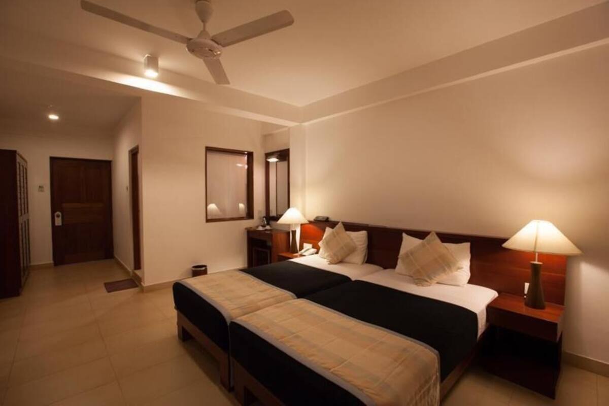 A hotel room with two beds, a ceiling fan, bedside lamps, a nightstand, and a mirror on the wall.