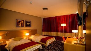 A hotel room with two beds, a desk, a mirror, and a red curtain.
