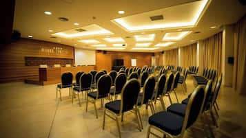 A hotel conference room with rows of chairs, a reception desk, and a large screen.