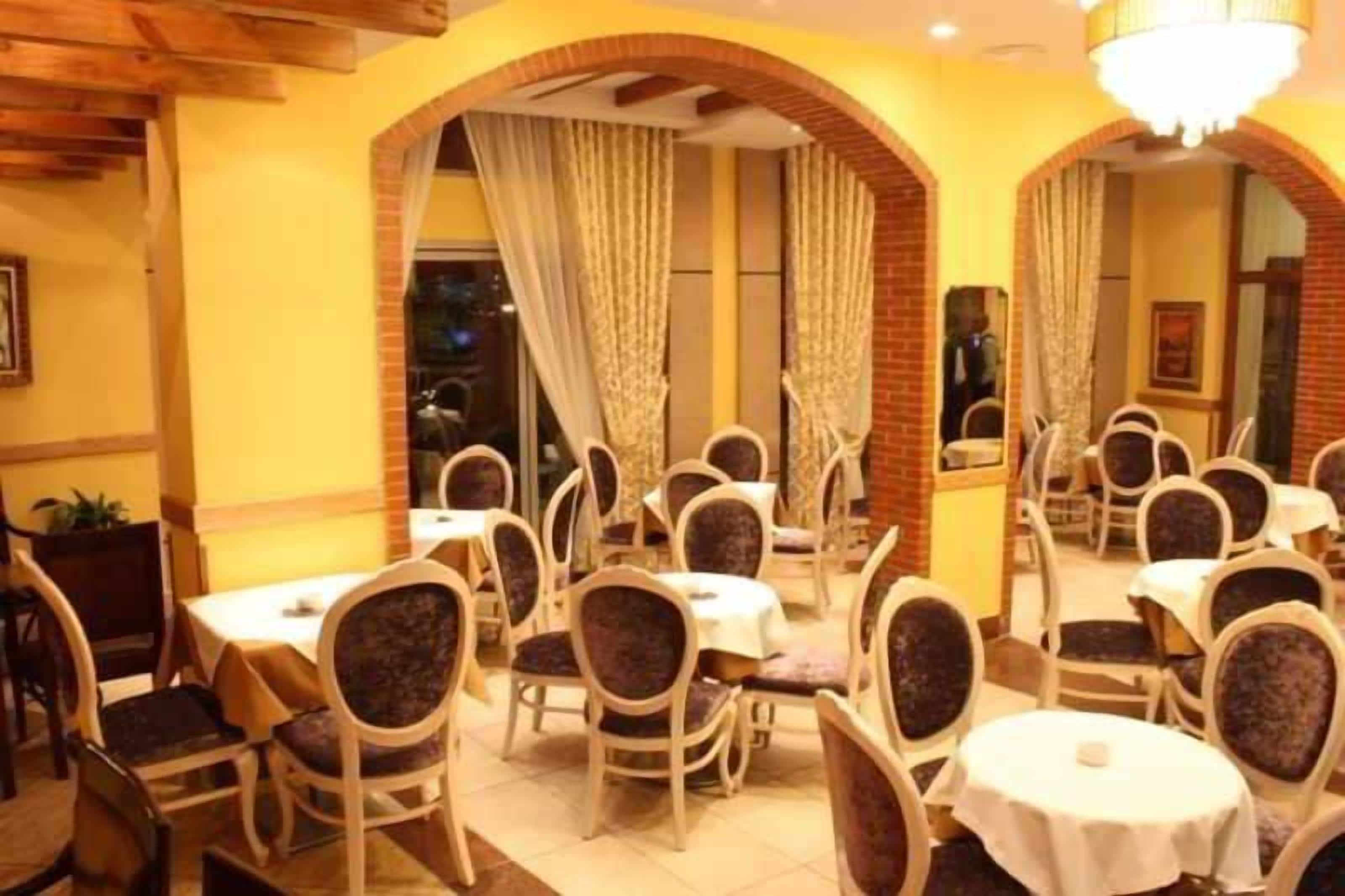 A restaurant with round tables and chairs, brick arches, and a chandelier.