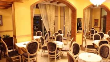 A restaurant with round tables and chairs, brick arches, and a chandelier.