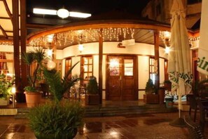 L’entrée d’un hôtel, avec une façade incurvée, des plantes en pot et un parasol.