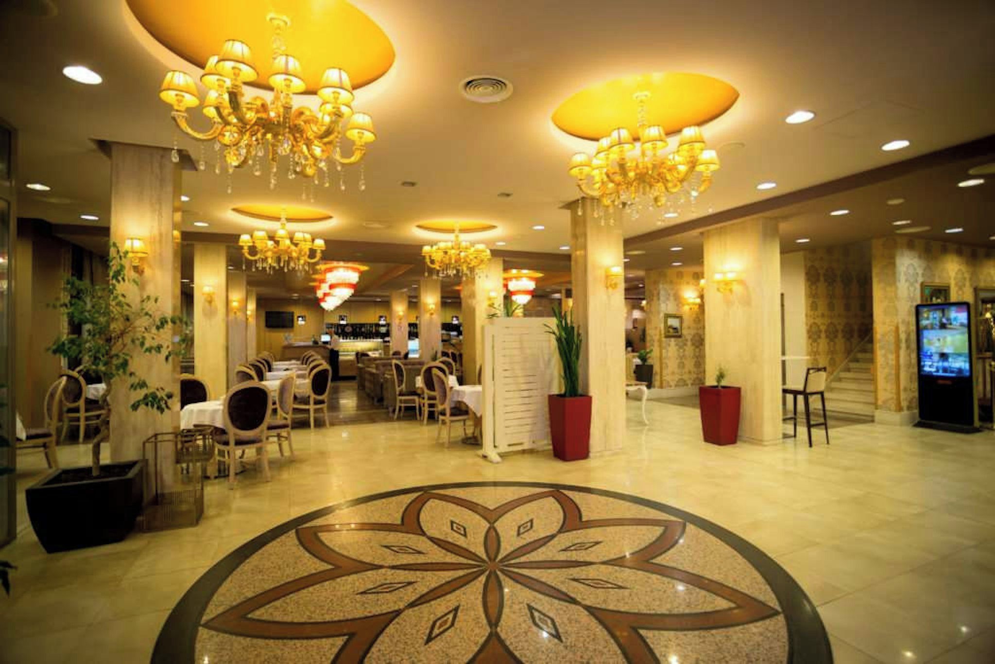 Vestíbulo de hotel con candelabros, áreas de descanso, una mesa de recepción y un amplio diseño decorativo en el suelo.