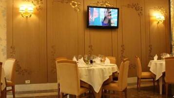 A dining area with tables set for four, a television mounted on the wall, and wall sconces.
