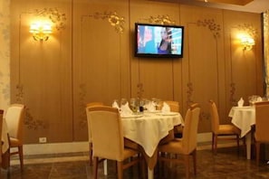 Un coin repas avec des tables disposées pour accueillir quatre personnes, un téléviseur fixé au mur et des appliques murales.