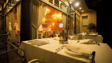 A dining area with a table set for two, a chandelier, and a view of the interior dining space.