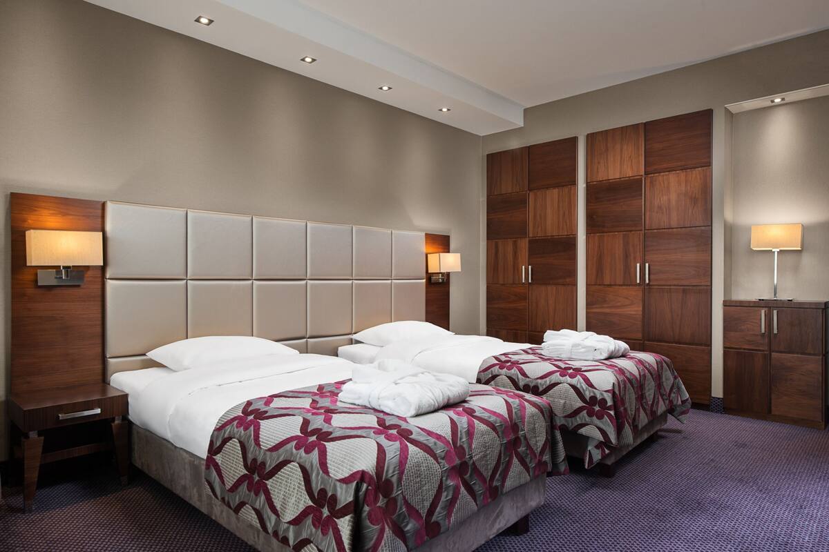 Une chambre d’hôtel avec deux lits, une grande armoire en bois et un petit bureau avec une lampe.