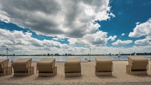 A beach with wicker lounge chairs aligned in rows, a calm body of water, and sailboats in the distance. - Hotel Warszawianka (Serock)